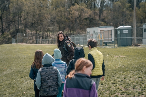 USFWS service employee in uniform leads a group of six elementary aged kids through a schoolyard for an environmental education program.