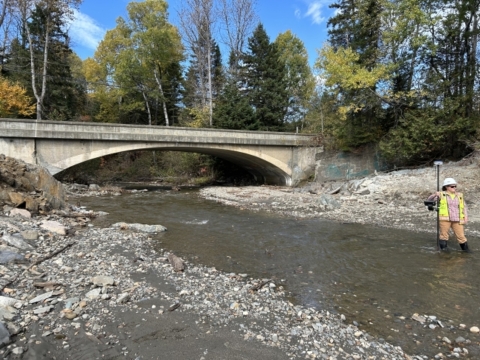 River in the foreground passing below a stone arched bridge in the background..