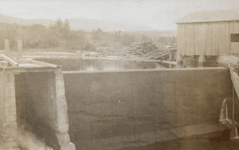 Large stone dam on a river and an elevated house next to it.