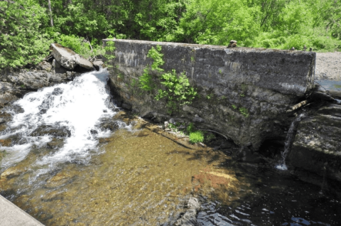 A stone dam in a river with rushing water on its side.