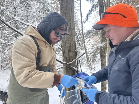 Image of 2 people in winter attire holding a bag and tube.