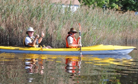 Two people in a yellow kayak. A ranger, in front, paddles while the USFWS volunteer in back gives a double thumbs-up.