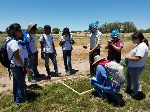 A group of individuals stand around a wood quadrant on a field