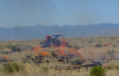 A small fire burns on a field with a vehicle behind it