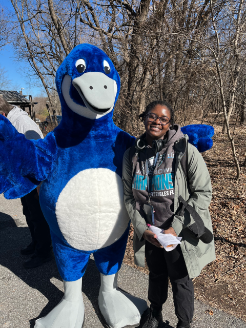 Woman standing next to a blue goose mascot.