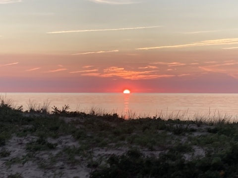 A view of the sun setting from a dune overlooking the ocean