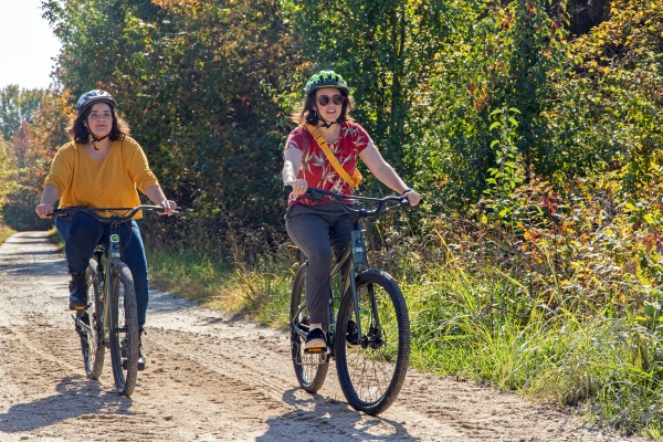 Two woman in bright clothing and helmets riding down a dirt road on electric assisted mountain bikes