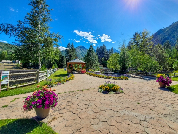 A wide-angle shot of pots and beds of flowers and a gazebo with mountains and blue sky in background.