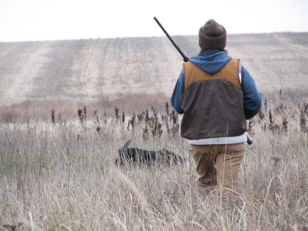 A hunter walking through grass with a dog