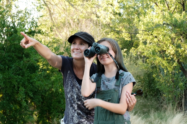 A woman points while a child next to her looks through binoculars