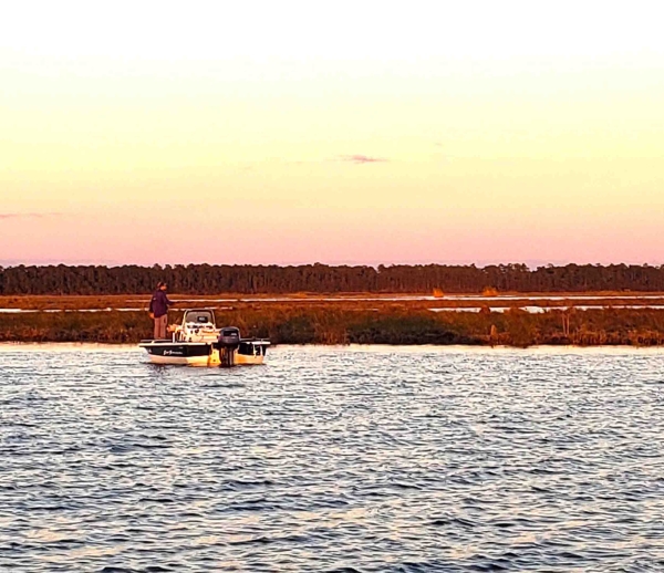 Person casting from a boat in a bayou at edge of marsh