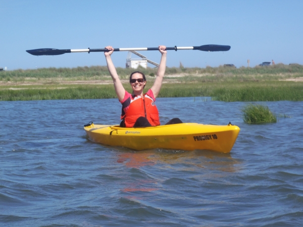 A kayaker smiles as they hold their paddle over their head