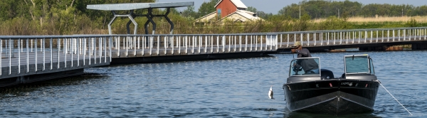 A fishing pier stretches into the river while an angler catches a fish from a boat nearby.