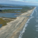 Aerial view of thin coastal barrier with ocean breach.