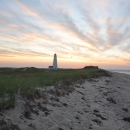 Sandy barrier island beach at sunset with lighthouse in the distance.