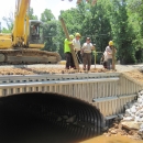 A construction crew stands atop a newly-installed culvert