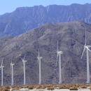 A row of wind turbines with mountains in the background.