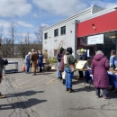 Community members standing in front of building collecting seeds. 