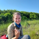 fish and wildlife biologist sits in the marsh holding a sparrow 