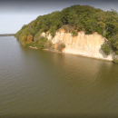 White cliffs capped with bright green trees. The cliffs are adjacent to a wide river. 