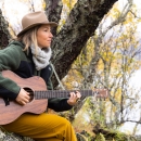 A woman sits in a tree and plays guitar