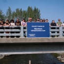 a group of people standing on a bridge over water holding a blue sign