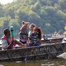 A man is fishing in a boat with three young girls. The kids are excitedly pulling a fish out of the water. 