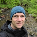 a man in a blue hat stands outside near a stream