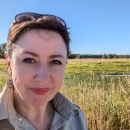 Smiling person with sunglasses on head stands in front of wetlands. 