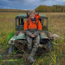 A person sits on a frame of an old jeep in the middle of a field.