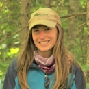 woman with dark hair smiles in front of green trees