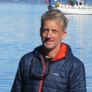 David Hand in a blue puffer jacket with a fishing boat in the background