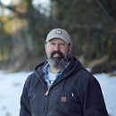 man in a fws hat and jacket standing in the snow with trees behind