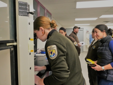 Woman in usfws uniform looks through microscope