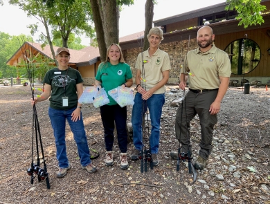 Four adults standing outside next to a building while holding fishing poles and tackle boxes.