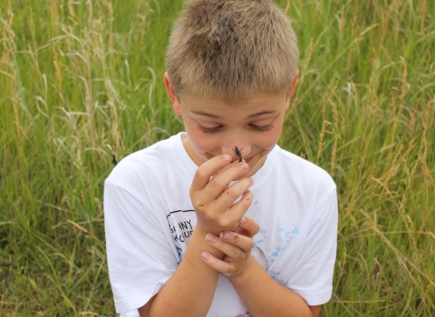 A smiling boy lets a crayfish crawl on his nose