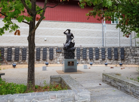 A stone courtyard with a statue in the middle and name plaques on a stone wall