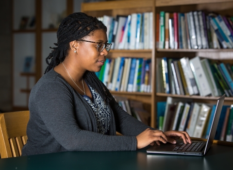 Liberian working on laptop with bookshelf in background