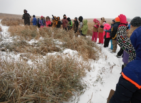 A teacher and a line of her students on a curved trail in the snowy prairie