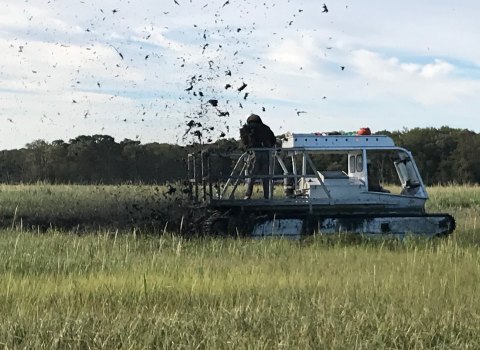 FWS staff using what looks like an atv with tank treads to cut through the marsh and carve the earth to create runnels. 