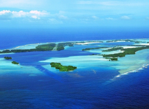 Aerial view of an island atoll surrounded by sandy reef in the deep blue ocean