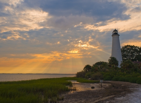 The Historic St. Marks Lighthouse with a backdrop of a beautiful orange and blue sunset over Apalachee Bay.