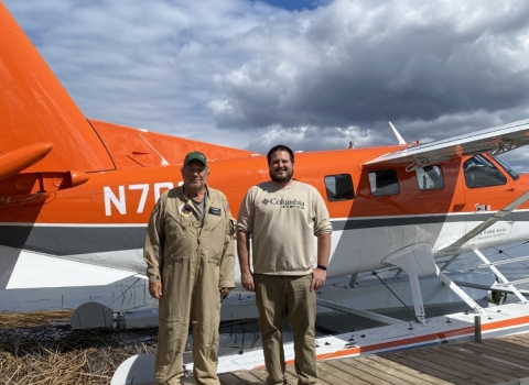 2 people stand in front of an airplane