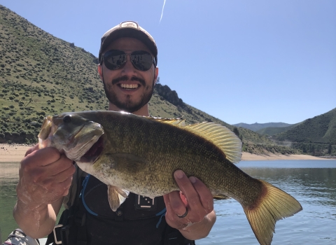 A man hold a fish while standing in a boat.