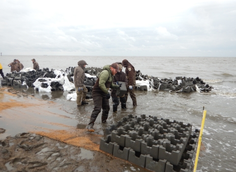 3 people stack concrete structures in shallow water