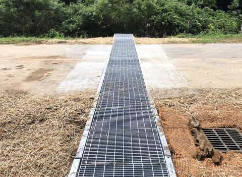 Metal grate running across a road with adjacent ground covered in straw.