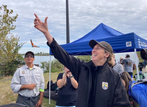 Woman wearing jacket with U.S. Fish and Wildlife Service logo releasing a butterfly