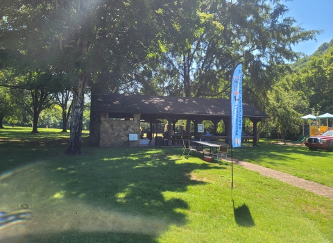 Park picnic area in a grassy meadow with lush green trees and a national fish hatchery banner