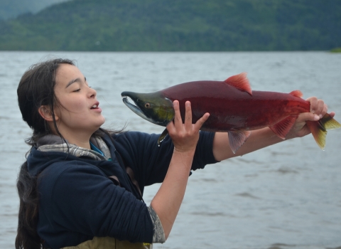 Aquatic Science Academy student holds a red salmon in front of her face. 