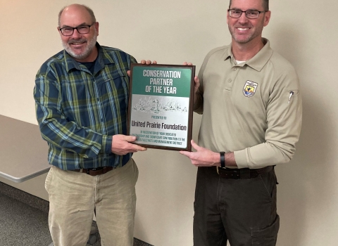 Two adults stand side by side holding an award plaque between them